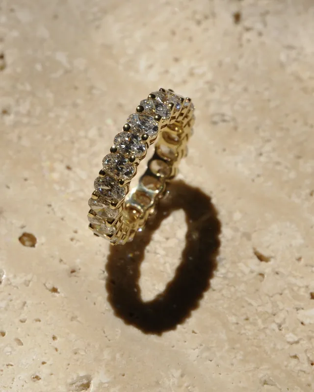 An eternity ring set with oval diamonds, standing on travertine in sunlight